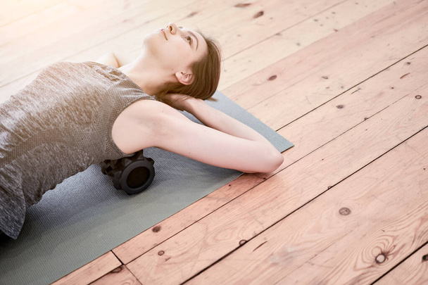 Woman doing yoga lying on massager on mat on wooden floor in gym - Valokuva, kuva