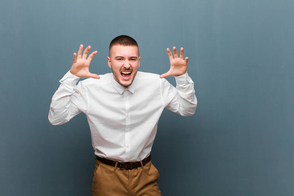 young handsome businessman screaming in panic or anger, shocked, terrified or furious, with hands next to head against flat background - Photo, Image