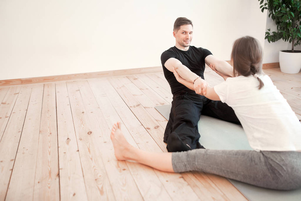 Man and woman in stretching while sitting on gray rug in studio with wooden floor in afternoon - Foto, immagini