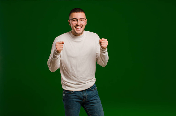 young handsome man feeling shocked, excited and happy, laughing and celebrating success, saying wow! against flat background - 写真・画像