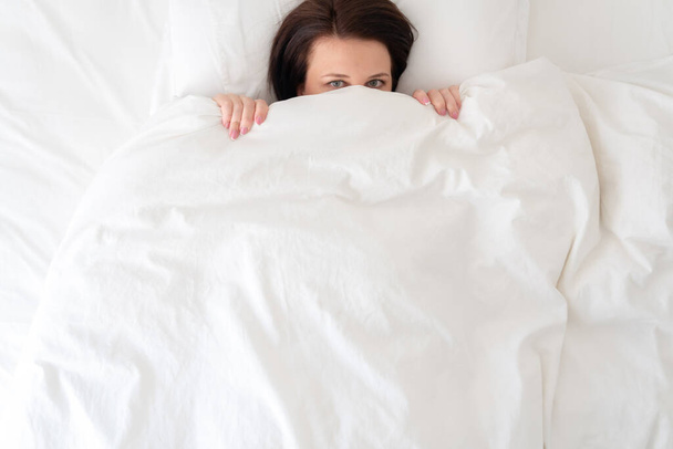 mladá krásná žena v posteli skrývající se pod peřinou - Fotografie, Obrázek