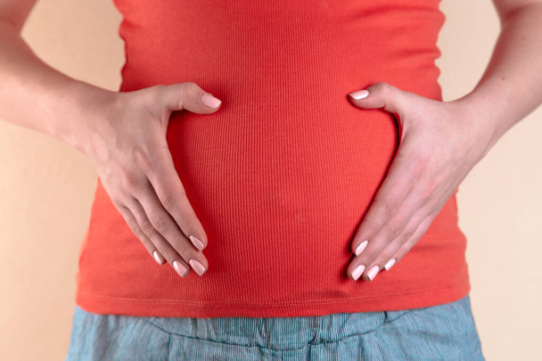Una vista de cerca del vientre de una mujer embarazada en una camiseta roja
 - Foto, imagen