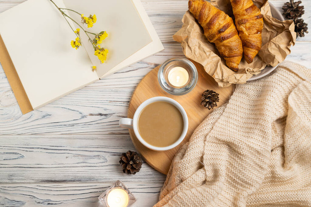 Hygge composition with coffee, candles, fresh croissants and knitted plaid. Overhead flat lay - Photo, Image
