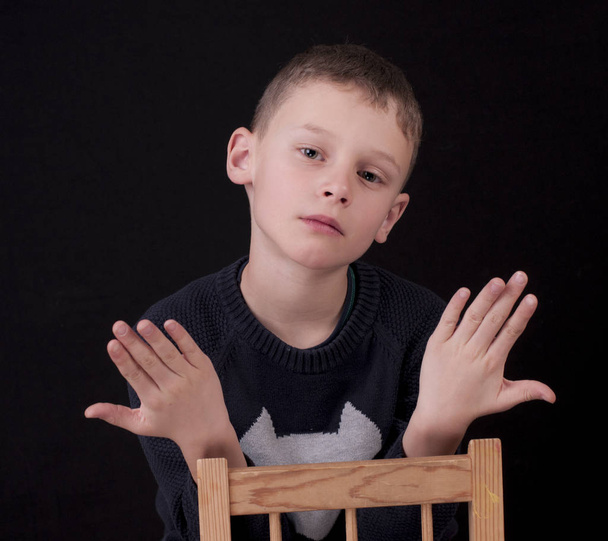 Chlapec sedí na židli a zvedá ruce. - Fotografie, Obrázek