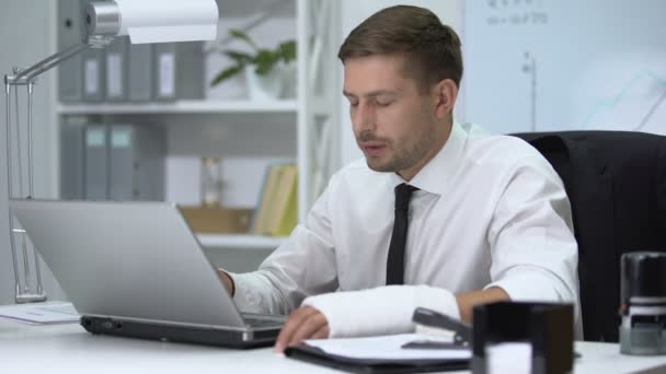 Workaholic man with broken arm in gypsum typing one hand on laptop pc, trauma - Кадры, видео