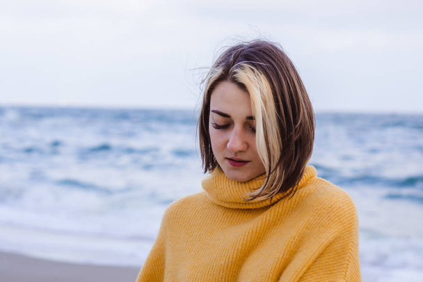 portrait of beautiful young woman in yellow pullover sweater on the beach - 写真・画像