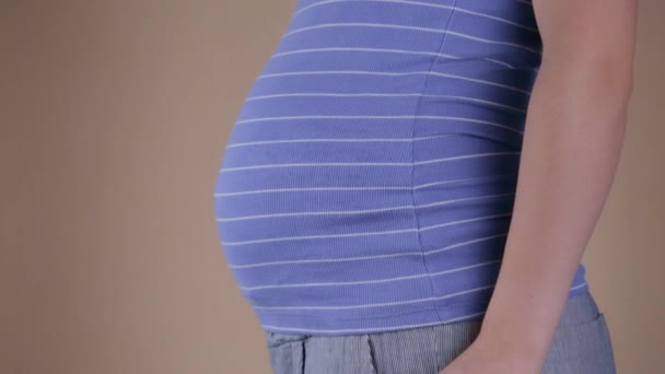 Een close-up van de buik van een zwangere vrouw in een blauw T-shirt, die in haar handen folders met de inscripties reizen en Ja. Reisconcept tijdens de zwangerschap. - Video