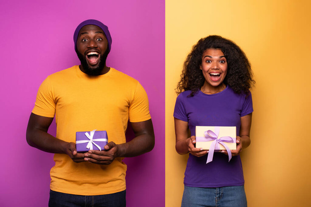 Pareja feliz y alegre muestran su regalo de Navidad. Fondo violeta y amarillo
 - Foto, Imagen