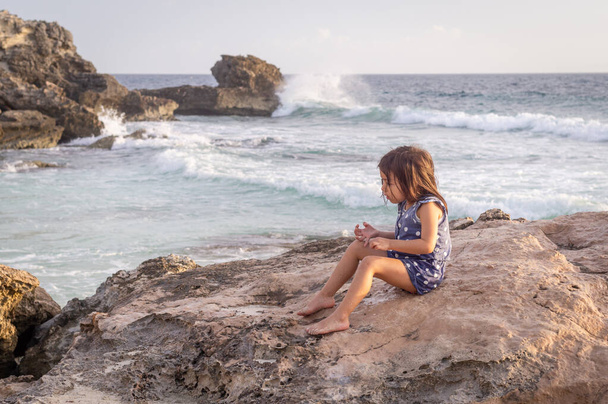 Menina de três anos em uma rocha no mar do Caribe
 - Foto, Imagem