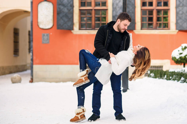 Attractive girl and her gorgeous boyfriend having fun on a date in a winter snowy street. Winter holidays concept. - Foto, afbeelding
