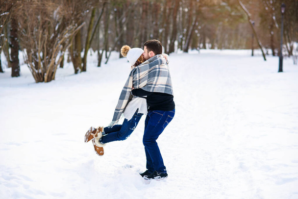 Young stylish couple in love have fun while walking on the snowy winter park. Handsome young man holds his beautiful girl on the hands. - Fotoğraf, Görsel