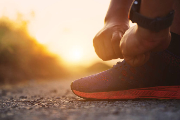 Close-up sportman tying sneakers with sunlight at sunset background. Runner and exercise concept. - Photo, Image