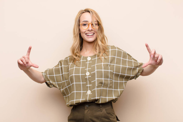 young pretty blonde woman framing or outlining own smile with both hands, looking positive and happy, wellness concept against flat color wall - Foto, Bild