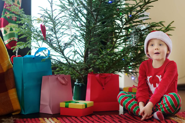 Excited little boy with a Christmas gift under fir tree at home. Portrait of happy kid in Christmas morning. - Fotó, kép