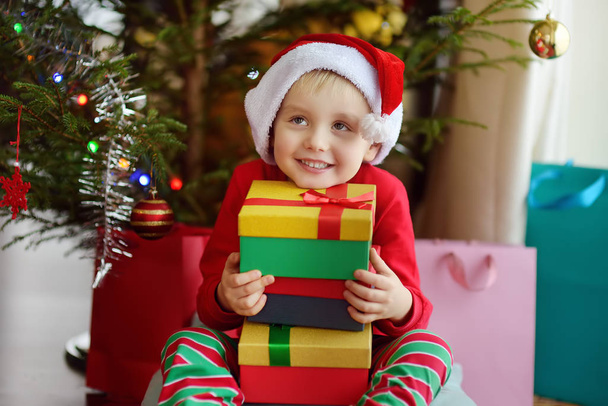 Excited little boy with a Christmas gift under fir tree at home. Portrait of happy kid in Christmas morning. - Photo, Image