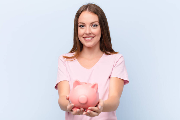 young red head woman  against flat wall with a piggy bank - Fotoğraf, Görsel