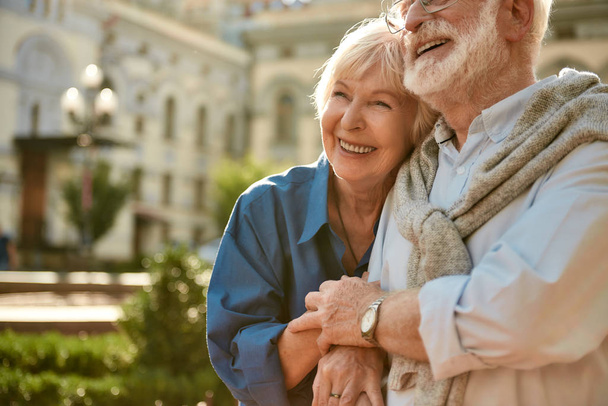 Πάντα μαζί. Ευτυχισμένο ζευγάρι ηλικιωμένων που δένεται μεταξύ τους και χαμογελά, ενώ περνούν χρόνο μαζί σε εξωτερικούς χώρους - Φωτογραφία, εικόνα