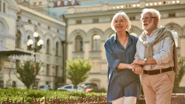 楽しい時間を一緒に。屋外を歩いている間に幸せと美しい高齢者のカップルの手を保持 - 写真・画像