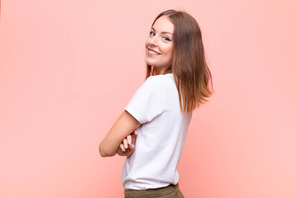 young red head woman smiling gleefully, feeling happy, satisfied and relaxed, with crossed arms and looking to the side against flat wall - Valokuva, kuva