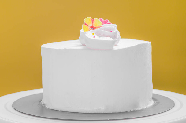 Isolated fresh cream frosted cake with flowers against yellow background - Photo, Image