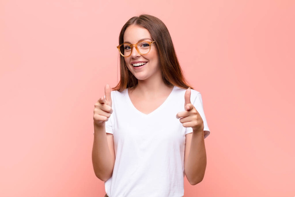 young red head woman smiling with a positive, successful, happy attitude pointing to the camera, making gun sign with hands against flat wall - Fotoğraf, Görsel