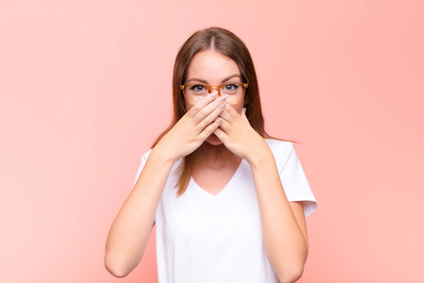 young red head woman covering mouth with hands with a shocked, surprised expression, keeping a secret or saying oops against flat wall - Foto, Imagen