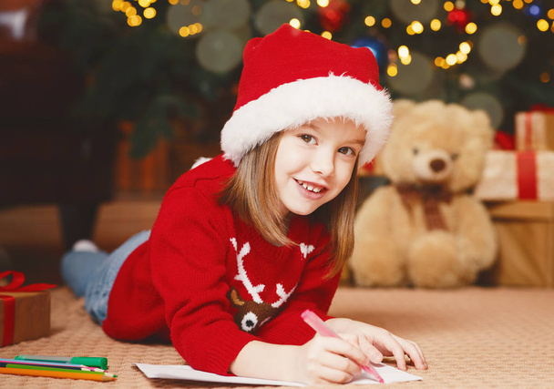Sorrindo menina em chapéu de xmas escrevendo carta para Santa
 - Foto, Imagem