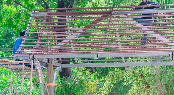 Saldatore e pittore stanno contribuendo a costruire una struttura del tetto a capanna sotto un grande albero di mango. - Foto, immagini