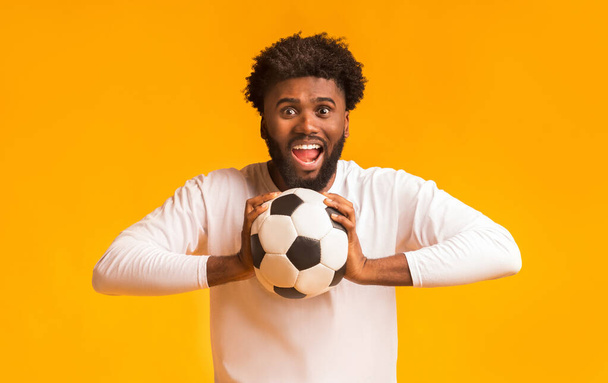 Football fan with ball full of emotions over orange background - 写真・画像