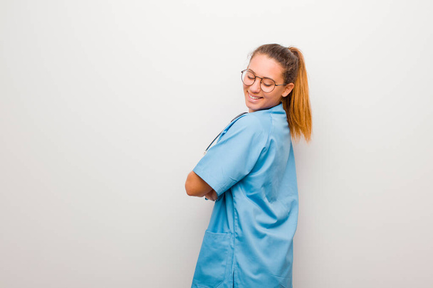 young latin nurse smiling gleefully, feeling happy, satisfied and relaxed, with crossed arms and looking to the side against white wall - Photo, Image