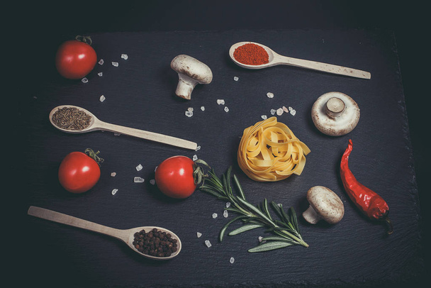 Raw pasta with vegetables, and spices on a black surface - Photo, image