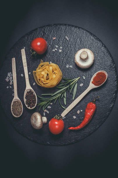 Raw pasta with vegetables, and spices on a black surface - Фото, зображення