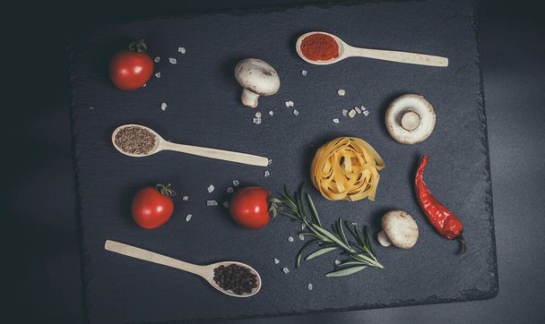 Raw pasta with vegetables, and spices on a black surface - Photo, Image