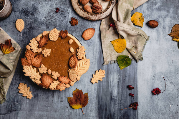 traditional pumpkin pie decorated with leaves shaped cookies on shabby blue background with textile, thanksgiving day concept - Foto, Imagem