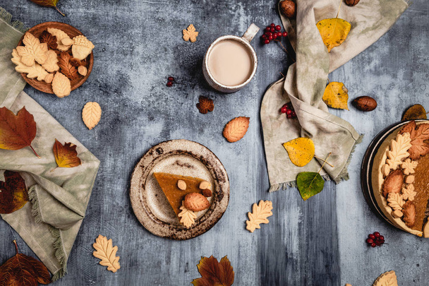traditional pumpkin pie decorated with leaves shaped cookies on shabby blue background with coffee and textile, thanksgiving day concept - Foto, Imagem