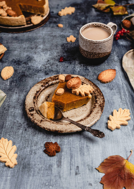 traditional pumpkin pie decorated with leaves shaped cookies on shabby blue background with coffee and textile, thanksgiving day concept - Фото, изображение
