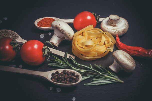 Raw pasta with vegetables, and spices on a black surface - Fotografie, Obrázek