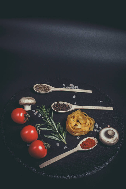 Raw pasta with vegetables, and spices on a black surface - Φωτογραφία, εικόνα