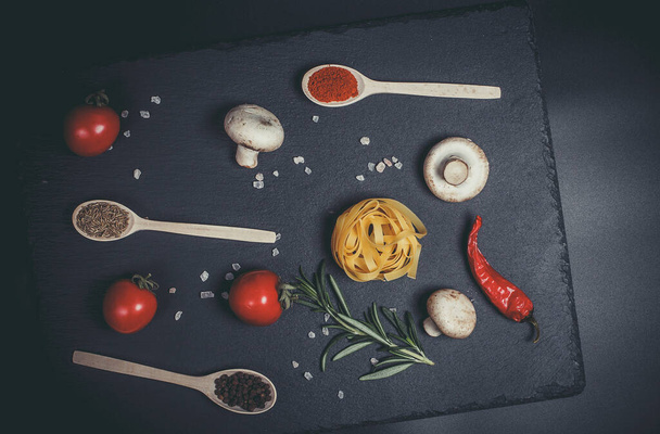 Raw pasta with vegetables, and spices on a black surface - Фото, зображення