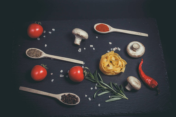 Raw pasta with vegetables, and spices on a black surface - Photo, image