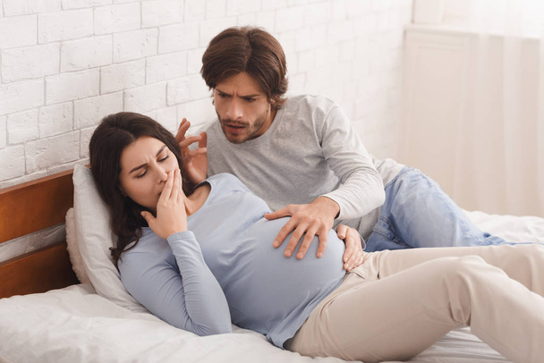 Schwangere leidet an morgendlicher Übelkeit, besorgter Ehemann beruhigt sie. - Foto, Bild