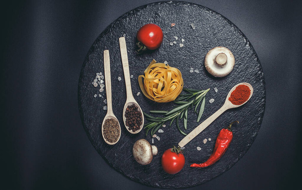 Raw pasta with vegetables, and spices on a black surface - Fotoğraf, Görsel