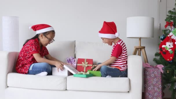 Kleine Kinder mit Weihnachtsmütze spielen an Heiligabend fröhlich im Wohnzimmer. - Filmmaterial, Video