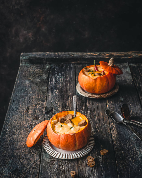 pumpkin soup with chili pepper and cheese crust in baked pumpkins on plates on wooden table - Foto, afbeelding