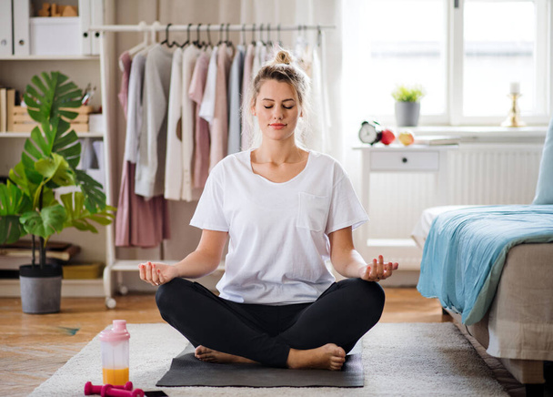 Young woman doing yoga exercise indoors at home, meditating. - Фото, изображение