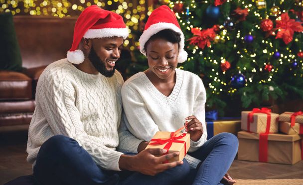 Black couple celebrating Christmas at home, unwrapping presents together - Valokuva, kuva