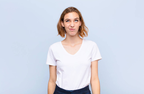 young blonde woman looking goofy and funny with a silly cross-eyed expression, joking and fooling around against flat color wall - Фото, изображение