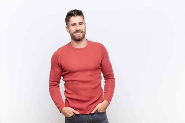 young handosme man smiling cheerfully and casually with a positive, happy, confident and relaxed expression against flat color wall - Foto, Imagen