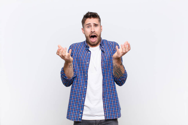 young handosme man looking desperate and frustrated, stressed, unhappy and annoyed, shouting and screaming against flat color wall - Fotoğraf, Görsel
