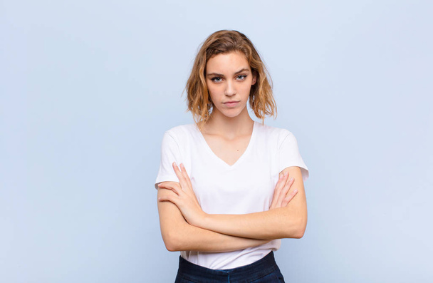 young blonde woman feeling displeased and disappointed, looking serious, annoyed and angry with crossed arms against flat color wall - Fotoğraf, Görsel